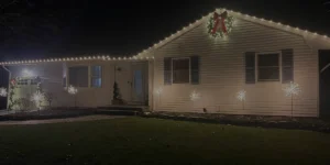 Christmas lights adorning a house exterior at night, featuring a wreath and illuminated decorations, showcasing festive outdoor design inspiration for landscape projects.