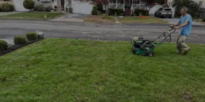 Man operating a lawn aerator on a well-maintained grassy yard, showcasing landscape maintenance services relevant to outdoor transformations.