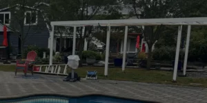 Pergola installation in a landscaped backyard with pool, featuring a ladder, chairs, and garden elements, highlighting Soft Wind's masonry and outdoor design expertise.