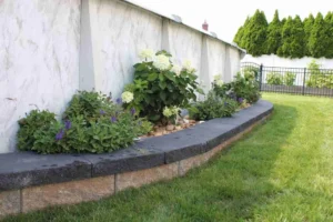 Lush garden design featuring flowering plants and a curved stone border along a wall, showcasing Soft Wind Landscape & Masonry's expertise in outdoor transformations.