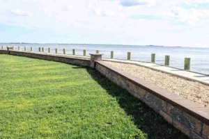 Landscape design featuring a manicured lawn and a stone masonry wall bordering a waterfront, showcasing Soft Wind Landscape & Masonry's expertise in outdoor transformations.