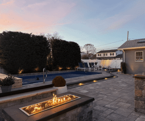 Luxury outdoor space featuring a stone patio, pool with lounge chairs, and a fire feature, showcasing Soft Wind Landscape & Masonry's design expertise in New York.
