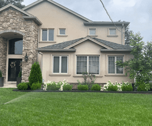 Modern residential architecture featuring stone masonry, landscaped front yard with green grass and blooming white flowers, showcasing Soft Wind Landscape & Masonry's design expertise.