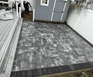 Paved gray patio with textured stone patterns beside a wooden deck, showcasing landscape and masonry work by Soft Wind Landscape & Masonry.