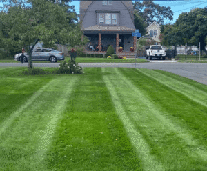 Lush green lawn with striped mowing patterns, showcasing a residential home and landscaped garden in New York, highlighting landscape design and masonry services by Soft Wind.