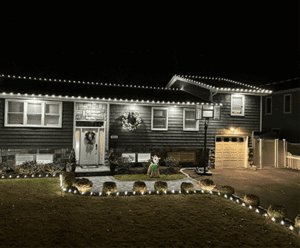 Residential landscape design featuring a beautifully lit home exterior with decorative lights and manicured lawn, showcasing masonry elements and inviting atmosphere, aligned with Soft Wind Gallery's landscape and masonry services in New York.