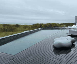 Modern outdoor pool with sleek wooden decking and contemporary lounge seating, surrounded by lush greenery, reflecting luxury landscape design by Soft Wind Landscape & Masonry.