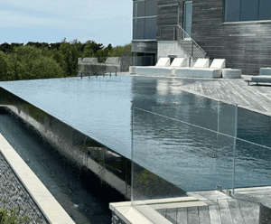 Modern infinity pool with glass edge and sleek patio, showcasing luxury outdoor design by Soft Wind Landscape & Masonry in New York.