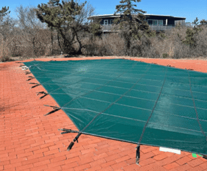 Green safety cover on red brick patio surrounded by trees, showcasing landscape design by Soft Wind Landscape & Masonry.