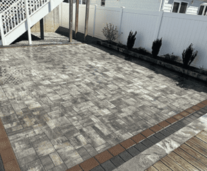 Paved outdoor patio featuring gray stone masonry, surrounded by a white fence and landscaping, highlighting Soft Wind Landscape & Masonry's design expertise.