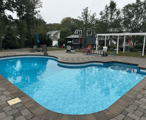 Luxury swimming pool with blue water, surrounded by patio area and outdoor furniture, showcasing landscape design by Soft Wind Landscape & Masonry.