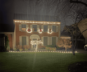 Elegant brick house decorated with holiday lights and wreaths, showcasing festive landscaping in a serene nighttime setting, reflecting Soft Wind Landscape & Masonry's expertise in outdoor design.