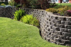 Curved stone retaining wall surrounded by lush greenery and landscaped garden, showcasing Soft Wind Landscape & Masonry's expertise in outdoor design.